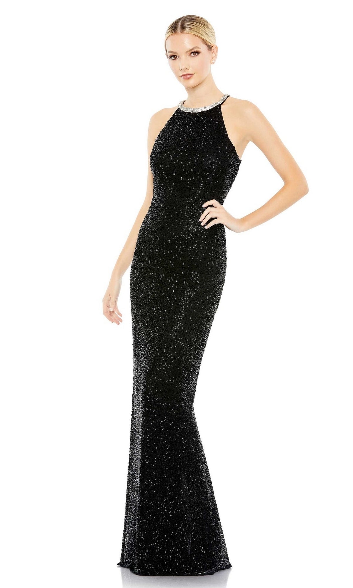 A woman poses against a white background in the Mac Duggal 93742, a long black beaded formal dress with a sleeveless design and high neckline.